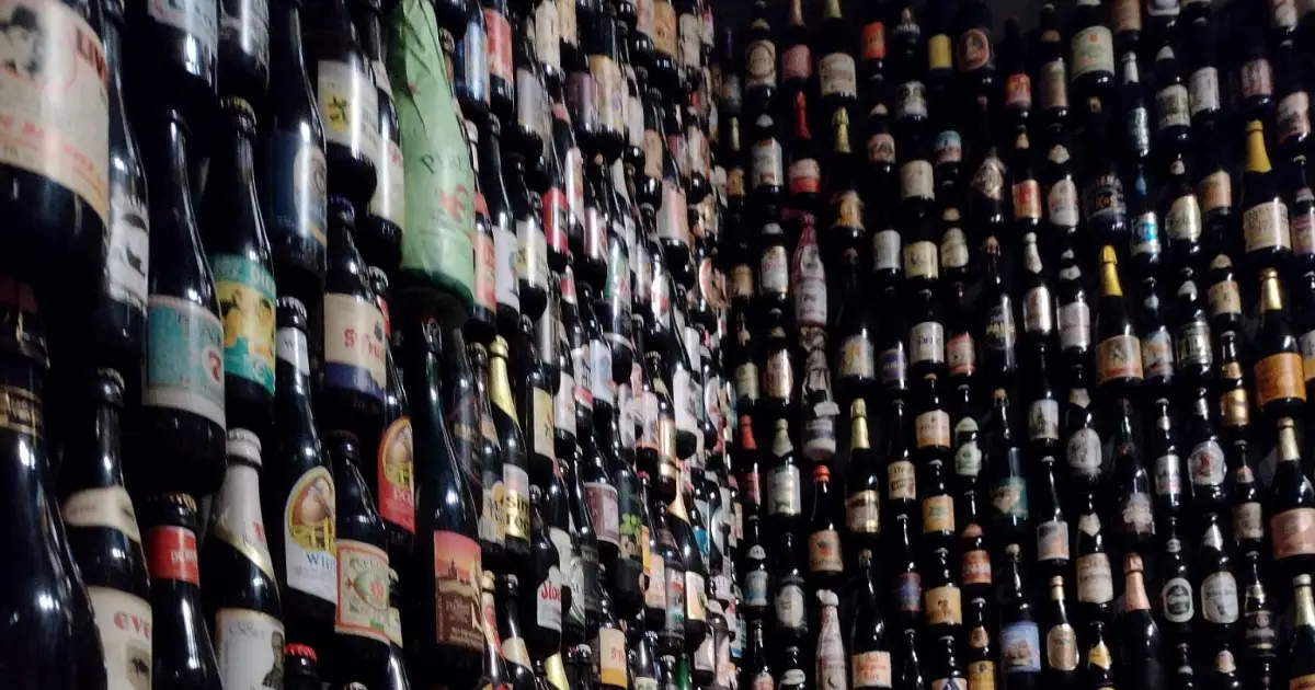 Reihen verschiedener Bierflaschen bedecken die Wände vom Boden bis zur Decke und bilden eine dichte, farbenfrohe Auslage in einem schwach beleuchteten Raum.